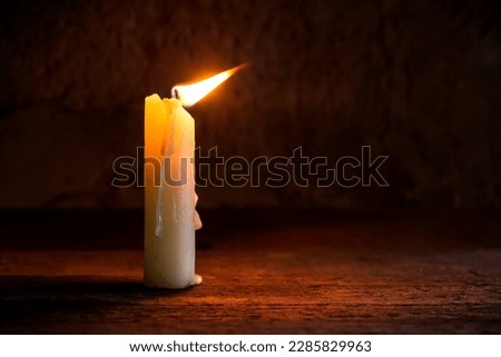 A lit candle in the breeze. A candle in the twilight. The flame of the candle fluctuates under the breeze.
