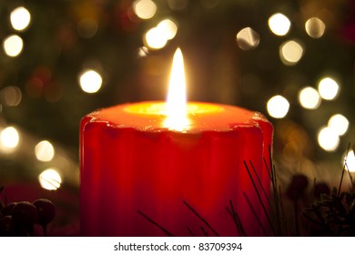 Lit Candle On Christmas Eve In Front Of The Diffused Lights On A Christmas Tree