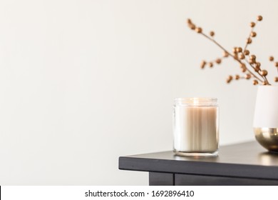 A Lit Candle On The Corner Of The Dresser Next To A Gold Plated Decoration Against A Cream Color Wall. Modern Interior Of A Bedroom, Aroma Therapy Candle 