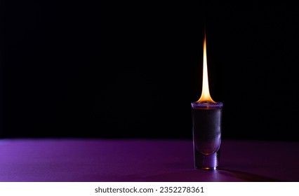 Lit candle in purple glass container with copy space on purple and black background. Flame, fire, colour and light concept.
