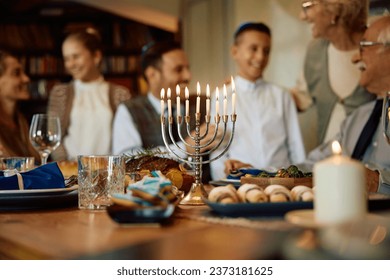 Encienden velas en menorah con la familia judía de multigeneración reunida para la celebración de Hanukkah.