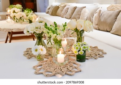 Lit Candles On A White Table, With A Centerpiece With Flowers, And On A Fabric