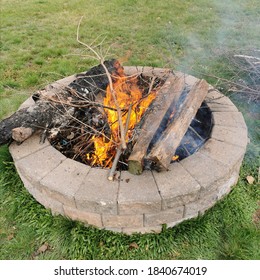 Lit Fire In A Circular, Outdoor Firepit Made Of Bricks. Logs Burning In A Backyard Campfire. 