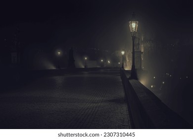 lit lamps on Charles Bridge and silhouettes of pedestrians and statues at night in the center of Prague 2021