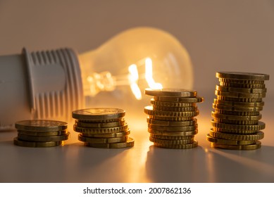 Lit light bulb with coins beside it. Increase in energy tariffs. Efficiency and energy saving. 
