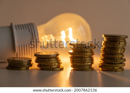 Lit light bulb with coins beside it. Increase in energy tariffs. Efficiency and energy saving. 
 [[stock_photo]] © 