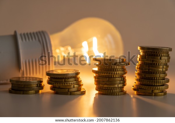 Lit light bulb with\
coins beside it. Increase in energy tariffs. Efficiency and energy\
saving. \
