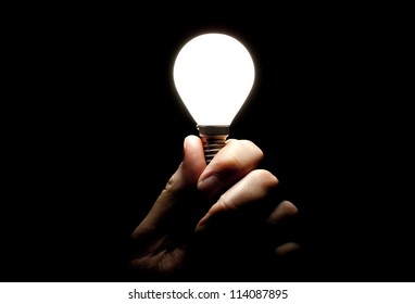 Lit lightbulb held in hand on black background - Powered by Shutterstock