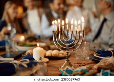 Lit menorah with multigeneration family in the background during Hanukkah celebration.