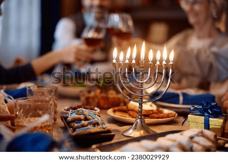 Lit menorah on dining table with Jewish family toasting while celebrating Hanukkah.
