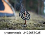 Lit mosquito coil spiral during nature retreat on camping site in forest. Outdoor fumigators - spirals with repelling scent and smoke that safe for environment and protect from insects in nature