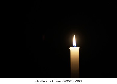A lit white candle in a black background, plenty of room for imagination