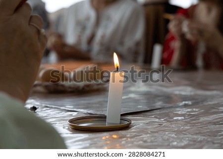 Lit white candle on a table during traditional pysanka workshop with fresh eggs and focused hands in background. Warm, serene atmosphere capturing cultural creativity and spring traditions
