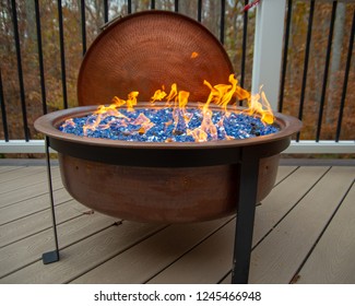 Lite Copper Fire Pit On A Poach With Fall Trees In The Background.