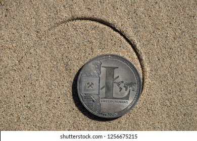 Litecoin cryptocurrency physical coin flipped on the backside placed on the sandy beach shore with the drawn Fibonacci spiral pattern