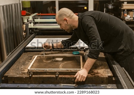Lithography artist holds a brush and working with a Lithographic limestone on a rolling press.