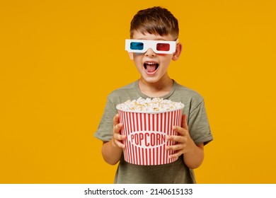 Littl surprised boy 6-7 years old in 3d glasses green t-shirt watch movie film hold takeaway popcorn bucket look camera isolated on yellow background studio portrait People emotions in cinema concept.