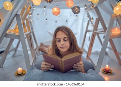 Little 10 Year Old Girl Reading Classic Book Under Her Home-made Tent Inside The Living Room.