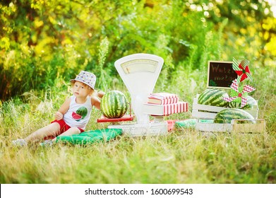 Little 3 Years Old Girl Play In Watermelon Seller With Big Old Fashioned White Scales. Emotional Kid Knock Big Watermelon In Park. Healthy Organic Food For Children. Watermelons In Summer Time