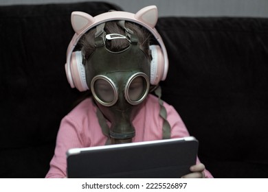 A Little 5 Year Old Girl In A Children's Gas Mask Plays A Tablet At Home On The Couch.