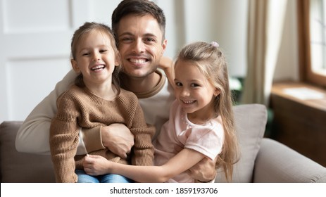 Little 6s 7s daughters sitting on daddy laps at home smile look at camera. Loving dad hugging pretty kids pose for picture, capture moment for family album. People celebrating Happy Father Day concept - Powered by Shutterstock