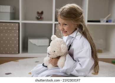 Little 6s Cute Girl In White Coat Play Veterinarian Use Stethoscope Listen Fluffy Toy Bear Heartbeat, Pretend Be Doctor, Sit On Floor In Nursery, Make Medical Check Up, Healthcare, Pediatrics