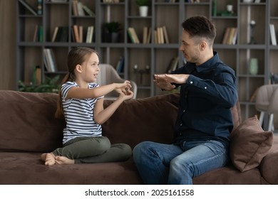 Little 7s deaf girl her father sit on couch speaking without words showing visual manual gestures using symbols. Professional speech therapist teach child. hearing impairment, communication concept - Powered by Shutterstock