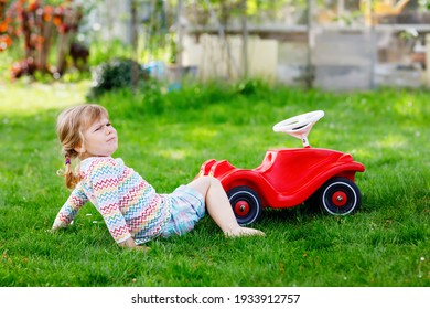 Little Active Adorable Toddler Girl Falling Down From Toy Car, Having Pain And Crying, Outdoors. Upset Child On Summer Day. Injured Hurt Kid In Gaden