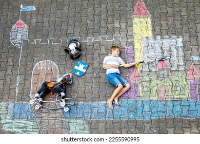 Little active kid boy drawing knight castle and fortress with colorful chalks on asphalt. Happy child in helmet and with spear having fun with playing knight game and painting - Shutterstock ID 2255590995