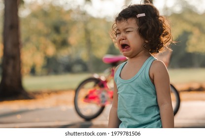 Little adorable angry caucasian curly hair girl standing outdoor in garden in summer holiday at evening, crying with sadness, depression of hurt and pain with copy space. Education and Kid Concept