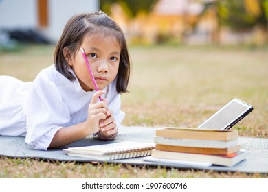 Little Adorable Asian Kid Lying Down On Mat Writing On Notebook, Concept Of Outdoor Education, A Girl Doing Her Homework, Kid Like Reading Book