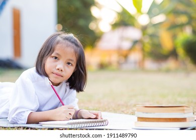 Little Adorable Asian Kid Lying Down On Mat Writing On Notebook, Concept Of Outdoor Education, A Girl Doing Her Homework, Kid Like Reading Book