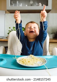 Little Adorable Baby Sit On Chair And Hands Up With Spaghetti While Eating And Smile