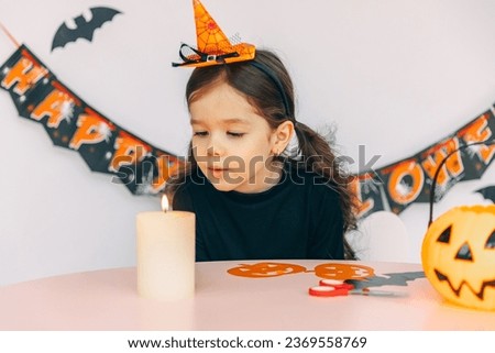 Little adorable cute Caucasian girl with curly hair playing and blowing candle with fun and amusement, celebrating Halloween party at home on decorated background. Kids Activity Concept
