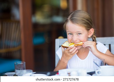 Little Adorable Girl Eating Bread With Butter And Honey On Breakfast