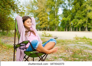 Little Adorable Girl Relaxed And Happy, Sitting On A Folding Chair For Travel