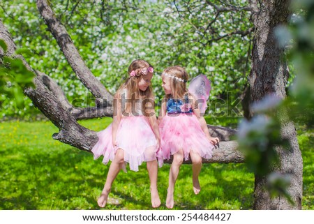 Little adorable girls sitting on blossoming tree in apple garden