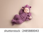 Little adorable newborn baby girl sleeping in a hat with dragon ears. Neutral background. Studio shot of a ten-day-old newborn baby. Beginning of life. Fairy tale.