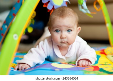 Little adorable newborn infant baby girl lying on tummy on colorful carpet with toys and looking in camera