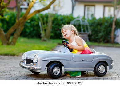 Little Adorable Toddler Girl Driving Big Vintage Toy Car And Having Fun With Playing Outdoors. Crying Sad Upset Child On Warm Summer Day. Hysteric Kid Playing In Domestic Garden