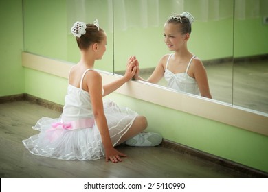 A little adorable young ballerina in a white tutu near the mirror - Powered by Shutterstock