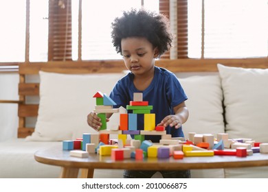 Little African american boy building a small house with colorful wooden blocks in living room at home. Educational toys for preschool and kindergarten children.
