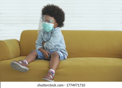 A Little African American boy wearing face mask and face shield sitting on yellow sofa at home, white background                 - Powered by Shutterstock