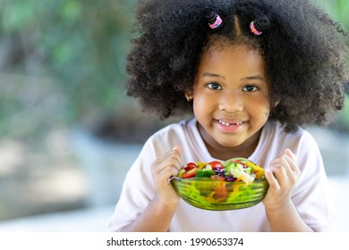 Little African American curly-haired girl sits and eats vegetables. delicious salad on the table merry Healthy food with nutritious nutrients to the body. Childhood and eating concepts. - Powered by Shutterstock