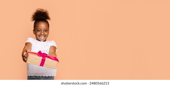 A little African American girl with a big smile holds out a gift wrapped in brown paper and a pink ribbon. She is wearing a white shirt and jeans, and her hair is pulled back in a high ponytail. - Powered by Shutterstock