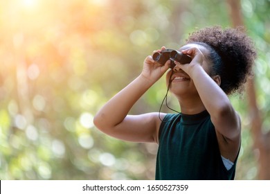 Little African American Girl with Binoculars during Hiking in Forest. Happy Kid playing Outdoors in Summer day. Girl Using binoculars in the Jungle.