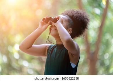 Little African American Girl with Binoculars during Hiking in Forest. Happy Kid playing Outdoors in Summer day. Girl Using binoculars in the Jungle.