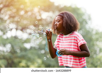 Little African American girl blowing soap bubbles in the park. - Powered by Shutterstock