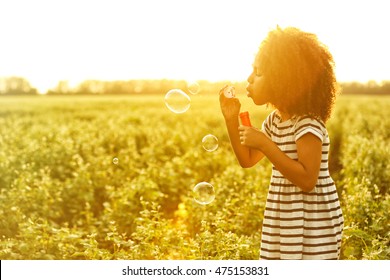 Little African American girl blowing bubbles in field