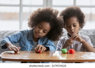 Little African American girl and boy kids have fun play with plasticine or modeling clay at home together. Small children siblings engaged in creative activity with colorful playdough, hobby concept - Powered by Shutterstock